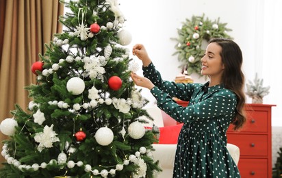 Young woman decorating Christmas tree at home