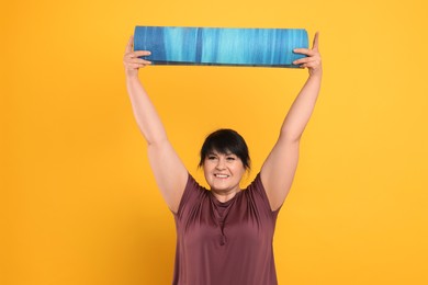 Happy overweight mature woman with yoga mat on orange background