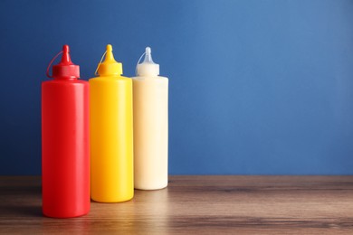 Ketchup, mustard and mayonnaise in squeeze bottles on wooden table against blue background, space for text