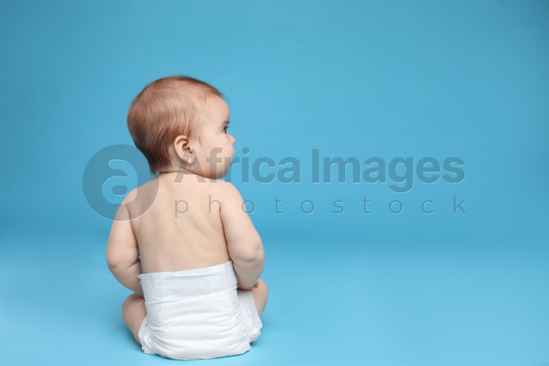 Cute little baby in diaper sitting on light blue background. Space for text