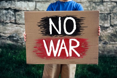 Boy holding poster with words No War against brick wall outdoors, closeup