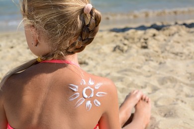 Little girl with sun protection cream on back near sea, closeup. Space for text