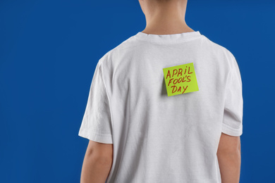 Preteen boy with APRIL FOOL'S DAY sticker on back against blue background, closeup