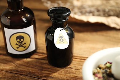 Open glass bottle of poison with warning sign on wooden table, closeup