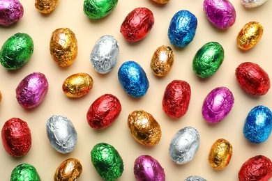 Chocolate eggs wrapped in colorful foil on beige background, flat lay