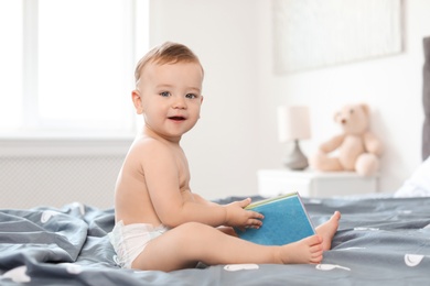 Photo of Adorable little baby with book on bed at home