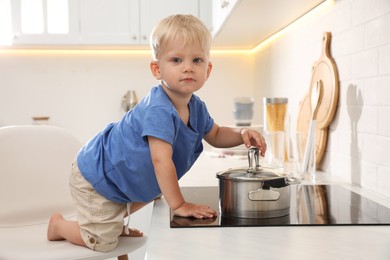Curious little boy playing with saucepan on electric stove in kitchen