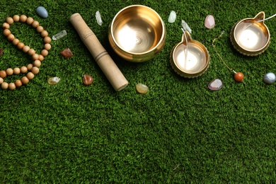 Flat lay composition with golden singing bowl on green grass, flat lay. Sound healing