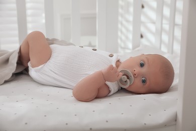 Cute little baby with pacifier lying on bed