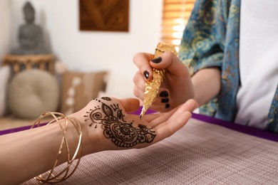 Professional mehndi master making henna tattoo indoors, closeup