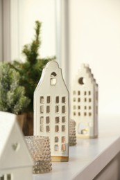 Photo of Beautiful house shaped candle holders and small fir trees on windowsill indoors
