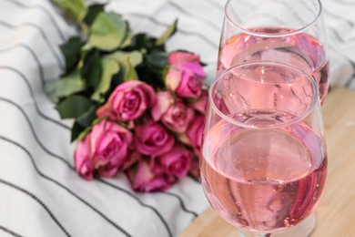 Photo of Glasses of delicious rose wine and flowers on white picnic blanket, closeup