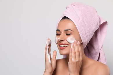 Beautiful woman applying facial cleansing foam on white background, space for text