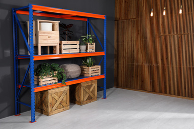 Metal shelving unit with wooden crates and different household stuff near black wall indoors. Space for text
