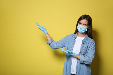Female volunteer in mask and gloves on yellow background, space for text. Protective measures during coronavirus quarantine