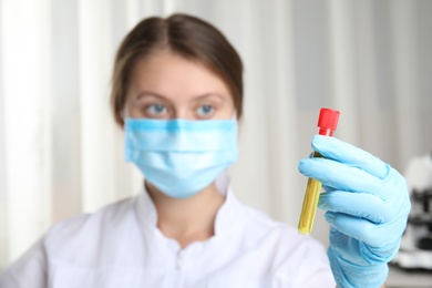 Doctor holding test tube with urine sample for analysis in laboratory, focus on hand