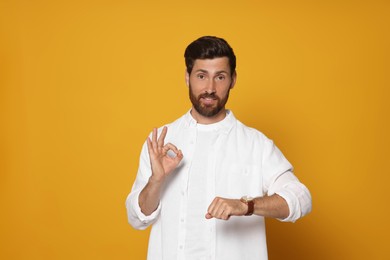 Photo of Bearded man with wristwatch showing ok gesture on orange background