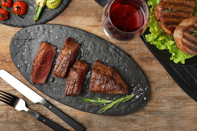 Delicious sliced beef tenderloin served on wooden table, flat lay