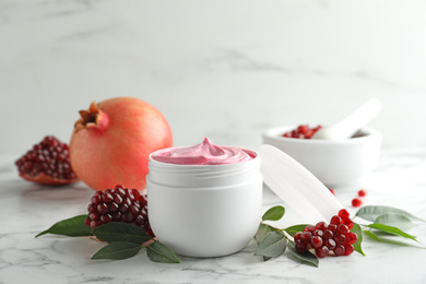 Fresh pomegranate and jar of facial mask on white marble table. Natural organic cosmetics