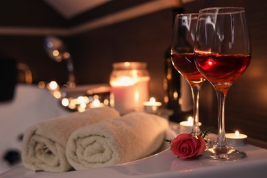 Glasses of wine, towels and rose on tub in bathroom, space for text. Romantic atmosphere