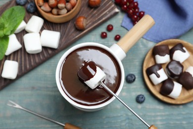 Dipping marshmallow into melted chocolate at blue wooden table, flat lay