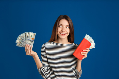 Happy young woman with cash money and wallet on blue background