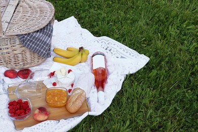 Picnic blanket with tasty food, basket and cider on green grass outdoors. Space for text