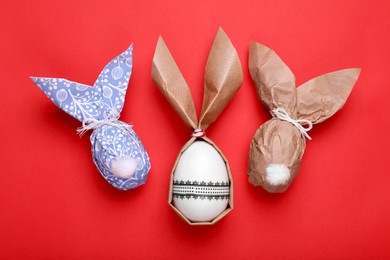 Photo of Easter bunnies made of craft paper and eggs on red background, flat lay