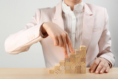 Businesswoman and stairs made with blocks on wooden table, closeup. Career promotion concept