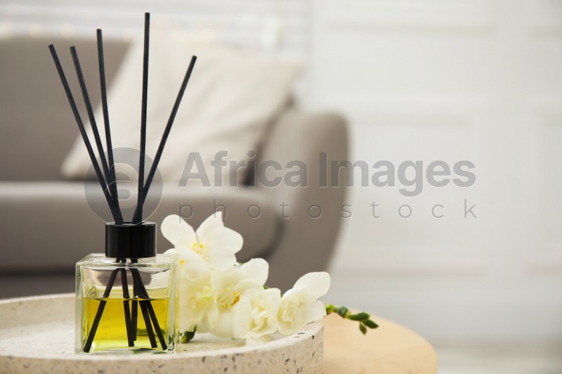 Reed diffuser with freesia on table in living room. Space for text