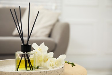 Reed diffuser with freesia on table in living room. Space for text
