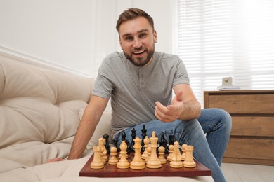 Happy young man playing chess on sofa at home