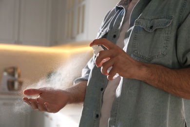 Man applying spray sanitizer onto hand in kitchen, closeup