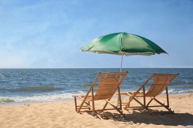 Green beach umbrella and deck chairs on sandy seashore