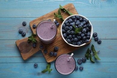 Photo of Glasses of blueberry smoothie with mint and fresh berries on turquoise wooden table, flat lay