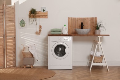 Laundry room interior with modern washing machine and stylish vessel sink on wooden countertop