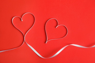 Hearts made of white ribbon on red background, flat lay. Valentine's day celebration