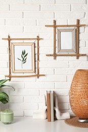 Photo of Decor elements and books on white table near brick wall with stylish bamboo frames