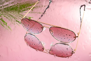 Stylish sunglasses with water drops on glass table