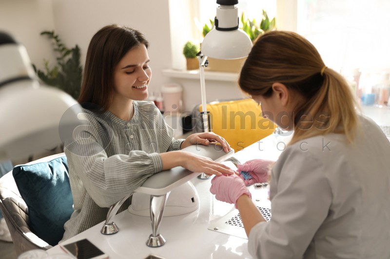 Professional manicurist working with client in beauty salon