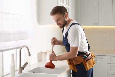 Plumber using plunger to unclog sink drain in kitchen
