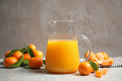 Jug of fresh tangerine juice and fruits on light table
