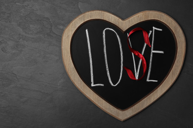 Heart shaped blackboard with word LOVE and letter S of red ribbon on dark background, top view. Composition symbolizing problems in relationship