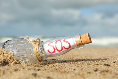 Glass bottle with SOS message in sandy beach, closeup