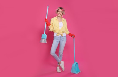 Young housewife with broom and dustpan on pink background