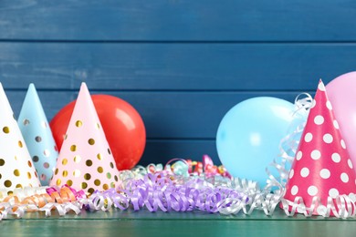 Colorful serpentine streamers, balloons and party hats on green wooden table. Space for text