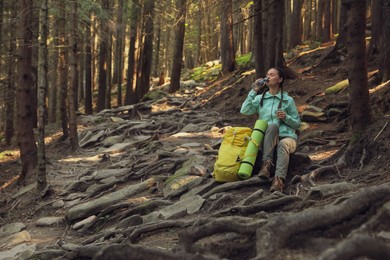 Tourist with backpack drinking water in mountain forest