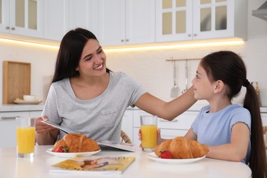 Happy mother and daughter having breakfast together in kitchen. Single parenting