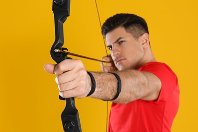 Man with bow and arrow practicing archery against yellow background, focus on hand