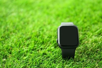 Stylish smart watch on green grass, closeup. Space for text